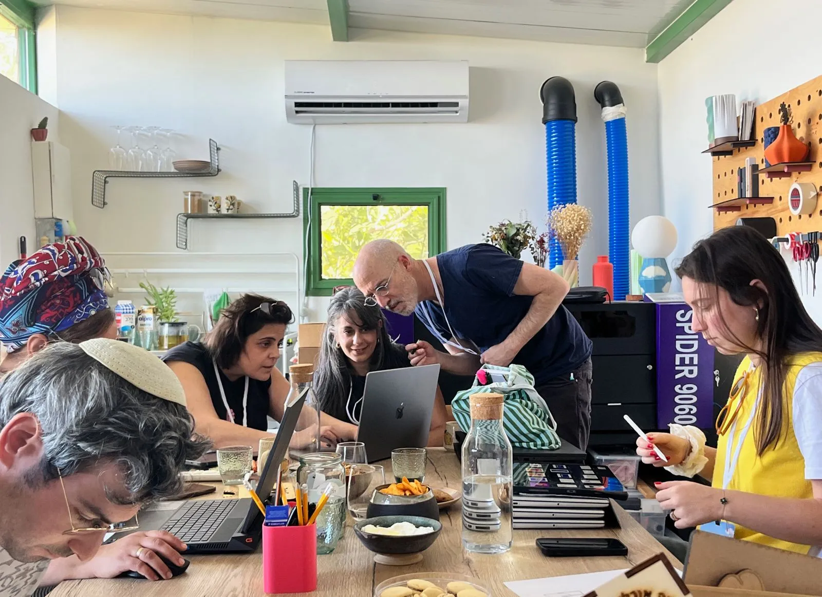 משתתפים בסדנה סביב שולחן העבודה בסטודיו, רוכנים יחד מעל מחשבים ניידים