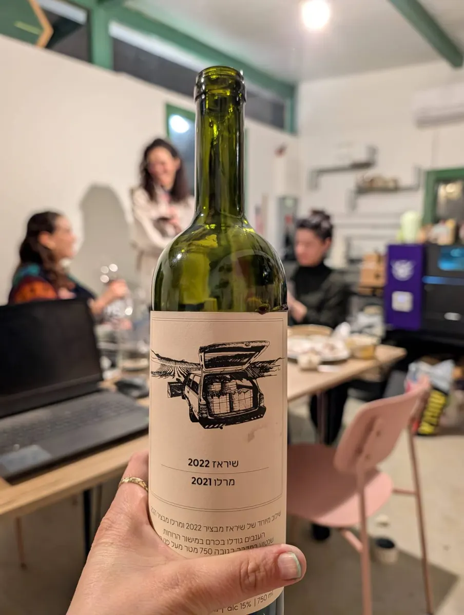 בקבוק יין מורם בערב Wine and Design בסטודיו, ומשתתפות יוצרות ברקע